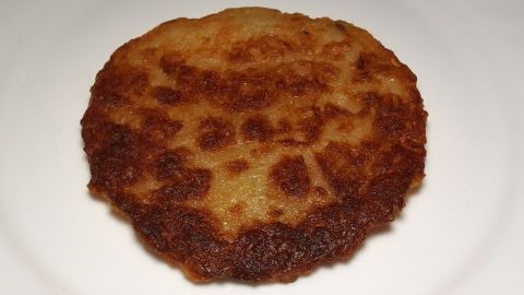 Ein fettarmer Kartoffelpuffer liegt auf einem weißen Teller und präsentiert seine goldbraune, knusprige Oberfläche.