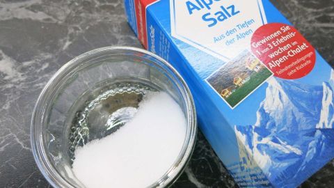 In einer Glasschale liegt Kochsalz, während eine blaue Verpackung mit der Aufschrift „Alpen Salz“ daneben steht.