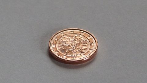Eine Kupfermünze liegt auf einem grauen Untergrund, symbolisiert die Methode zum Stoppen kleiner Blutungen.