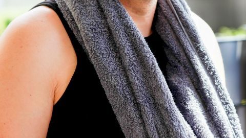 Mit einem nassen Handtuch, das anschließend für einige Minuten in das Gefrierfach gelegt wird, kannst du dich an heißen Sommertagen abkühlen. Ein Mann trägt ein graues Handtuch um den Hals, während er sich in der warmen Sonne entspannt und die Umgebung betrachtet.