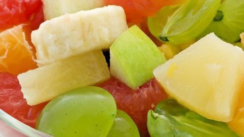 Eine Schüssel mit buntem Obstsalat zeigt frisch geschnittene Stücke von Trauben, Ananas und Äpfeln.