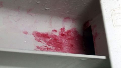 Textilfarbe an der Waschmaschine mit Nagelentferner entfernen. Ein Waschmaschinenfach ist stark mit roter Textilfarbe befleckt, das Wasser läuft herab und hinterlässt Spuren.