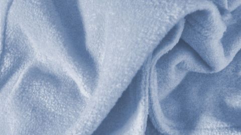 Eine blaue Decke liegt zerknittert auf einer Oberfläche und zeigt eine glatte Textur, die zur Entfernung von Schimmelflecken einlädt.
