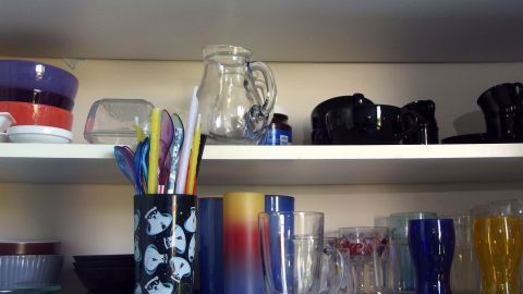 Regale mit Geschirr und Gläsern stehen ordentlich in einem Schrank, während eine Person Fotos für den Umzug macht.