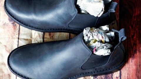 Stark verschmutzte Lederschuhe liegen auf einem Holztisch, mit Zeitungen zur Formstabilität im Inneren der Schuhe.