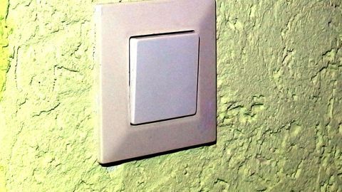 Ein Lichtschalter an einer strukturierten grünen Wand wartet darauf, gereinigt zu werden, um seine Vergilbung zu entfernen.