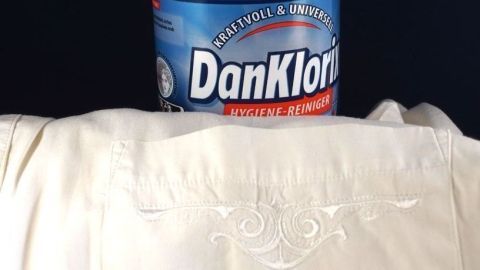 Eine Dose DanKlorix steht auf einem weißen Kleidungsstück, das mit Flecken behaftet ist, bereit zur Fleckenentfernung.