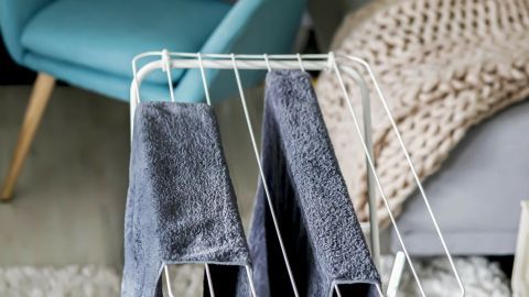 Du leidest unter Hitze und hast keine Klimaanlage? Kühle dein Zimmer mithilfe von feuchten Handtüchern und einem Ventilator. Ein Wäschegestell mit grauen Handtüchern steht in einem modernen Wohnzimmer, um den Raum kühl und luftig zu halten.