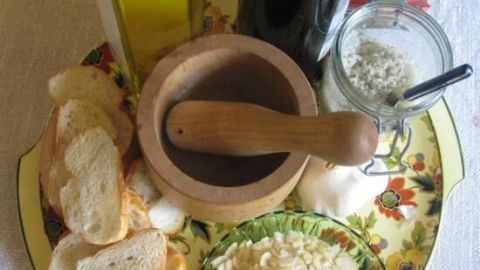 Auf einem bunten Teller liegen Zutaten für Skordalia: Brotstücke, eine Mörser, Ölflaschen und Mandelstückchen bereit.