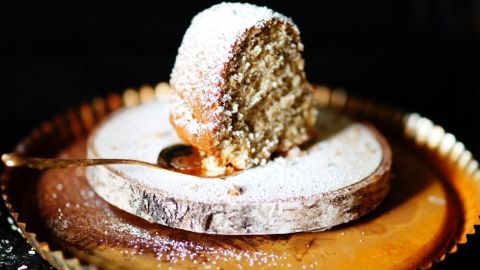 Nusskuchen mit Erdnussbutter verfeinern: So schmeckt das Gebäck noch intensiver nach feinen Nüssen. Ein Nusskuchen mit Puderzucker bestäubt liegt auf einem rustikalen Holzbrett, umgeben von einem glänzenden Teller.