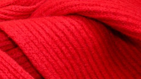 Ein rotes Wollstück liegt sanft gefaltet auf einem Tisch, bereit zum Glätten oder Aufrebbeln für ein Strickprojekt.