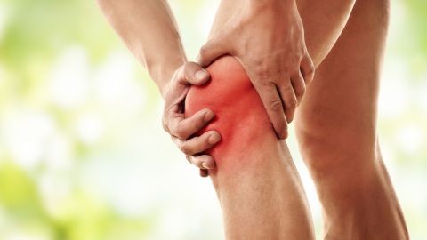 Eine Person hält sich schmerzhaft das Knie, während sie in einer grünen, natürlichen Umgebung steht. Arthrose kann helfen.