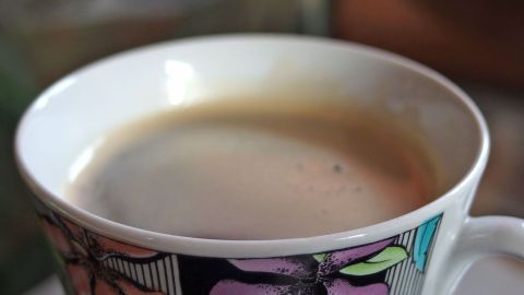 Eine Tasse mit Kaffee wird sorgsam gehalten, um das Kleckern während des Transports zu vermeiden.