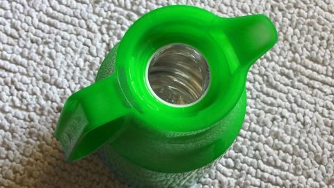 Eine grüne Thermoskanne liegt auf einem hellen, texturierten Untergrund und zeigt ihre Öffnung, ideal zum Befüllen.