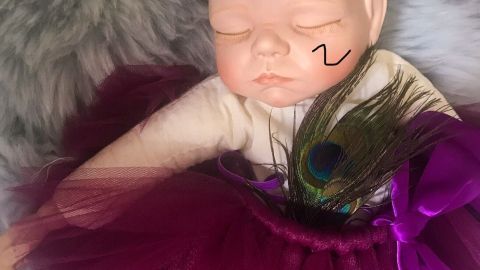 Eine Puppe mit einem lila Tutu und einer Krone liegt auf einem weichen Untergrund, mit einem Fleck im Gesicht.