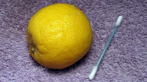 Eine frische Zitrone liegt neben einem Wattestäbchen auf einem weichen, lila Tuch, ideal für die Anwendung von Zitronensaft gegen Pickel.