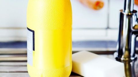 Eine gelbe Flasche mit Reinigungsmittel und ein Schwamm stehen in einer Edelstahlspüle, um die Spüle sauber zu putzen.
