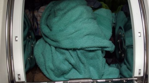 Ein großer, zusammengewickelter, grüner Handtuchhaufen befindet sich in einer Waschmaschine und wartet auf die Reinigung.
