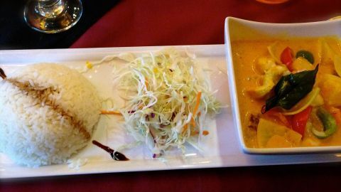 Weißer Reis und grüner Salat liegen neben einer Schale mit Thai-Curry, serviert auf einem roten Tisch.