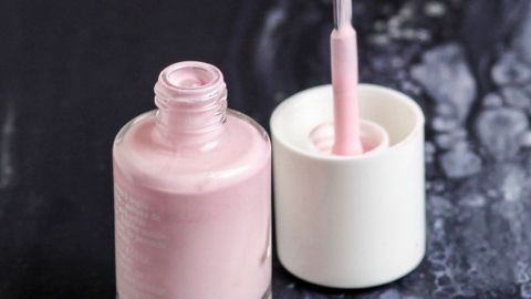 Eine flasche Nagellack steht offen auf einer dunklen Oberfläche, die Pinselspitze ist bereit zum Auftragen des rosa Lacks.