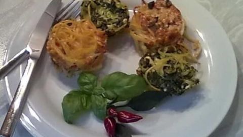 Auf dem Teller liegen goldbraune Tagliatelle aus der Muffinform, die appetitlich angerichtet zwischen frischen Kräutern sind.