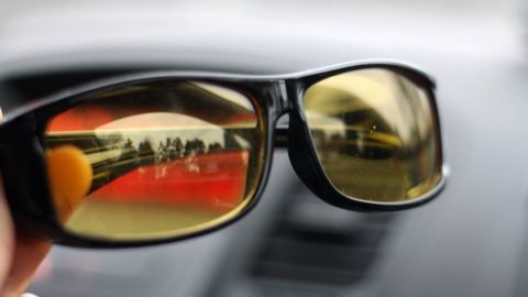 In der Hand gehaltene Sonnenbrille reflektiert eine verschwommene Umgebung, die vom Innenraum eines Fahrzeugs geprägt ist.