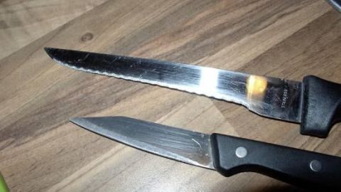 Zwei Messer liegen auf einer Holzoberfl&auml;che, das obere Messer hat eine gezackte Klinge, das untere eine glatte.