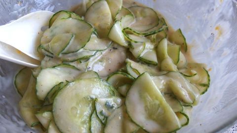 Gurkenstücke werden in einer Schüssel mit Dressing gemischt, um einen erfrischenden Salat zuzubereiten.