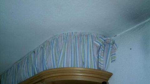 Ein Küchenhängeschrank ist mit einem gewebten Stoff dekoriert, der den Raum zwischen dem Schrank und der Decke ausfüllt und versteckt.