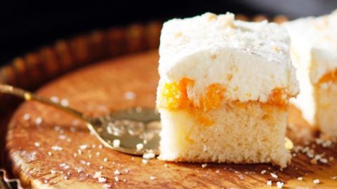 Ein Stück Schmandkuchen vom Blech liegt auf einem rustikalen Teller, umgeben von leichten Kuchenschnipseln und einer Gabel.