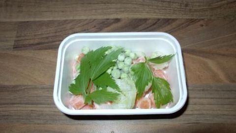 Eine Schüssel mit Tütensuppe wird verfeinert, umgeben von frischen Kräutern und Gemüse, auf einer Holzoberfläche.