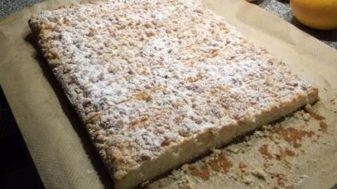 Ein Butterstreuselkuchen liegt auf Backpapier, bestreut mit Puderzucker, umgeben von Zitronen und einer Küchentheke.