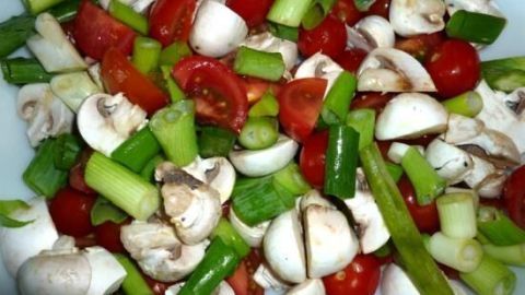 Ein buntes Gemüsegericht mit Kirschtomaten und Champignons, frisch geschnitten und angerichtet auf einem weißen Teller.