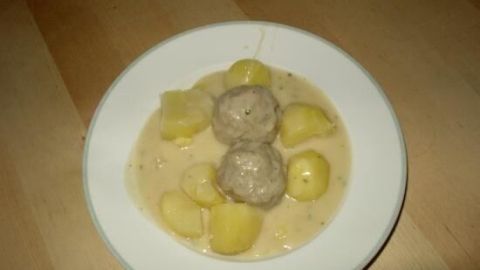 Ein Teller mit Königsberger Klopse liegt auf einem Tisch, umgeben von cremiger Sauce und Kartoffeln.