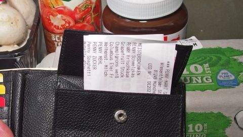 Eine Geldbörse hält einen Kassenbon, umgeben von Lebensmitteln im Supermarkt, um Sicherheit nach dem Kauf zu gewährleisten.