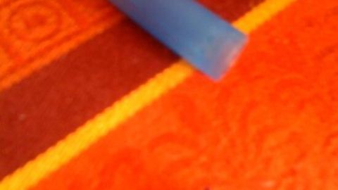 Ein blauer Tintenkiller liegt auf einer orangefarbenen Oberfläche, neben einem Stift, der für das Radieren benutzt wird.