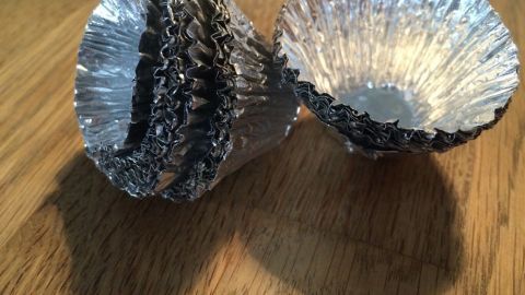 Zwei kleine, silberne Kerzenständer aus Aluminium stehen auf einem Holzuntergrund und wirken ungenutzt.