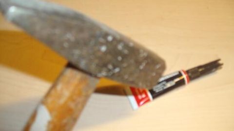 Ein Hammer liegt neben einer Tube Sekundenkleber, während er zum Öffnen verwendet wird, ohne dabei Gewalt anzuwenden.