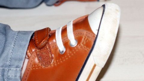 Braune Kinderschuhe stehen auf einem hellen Boden, bereit, gereinigt zu werden, während ein Kind in Jeans sitzt.