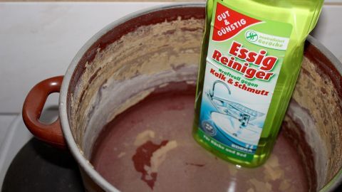 Mithilfe von Essigreiniger lassen sich Kalk- und Eiweissflecken hervorragend aus Kochtöpfen entfernen. Ein Kochtopf mit hartnäckigen Kalk- und Eiweißflecken. Essigreiniger steht in der Mitte des Topfes, bereit zur Anwendung.