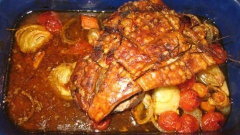 Ein saftiger Knoblauchbraten liegt in einer Auflaufform, umgeben von Gemüse in einer köstlichen Bratensoße.