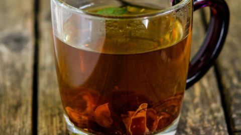 Ein Glas Tee steht auf einem Holztisch, während der Duft von Kräutern in der Luft schwebt und eine frische Minze daneben liegt.