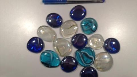 Bunte Glassteine liegen auf einer Oberfläche, während ein blauer Stift daneben liegt und die Dekoration umgibt.