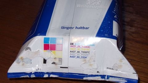 Ein gelber Sack ist gefaltet und bereit, Abfälle zu sammeln. Er liegt auf einer Holzoberfläche, umgeben von Alltag.
