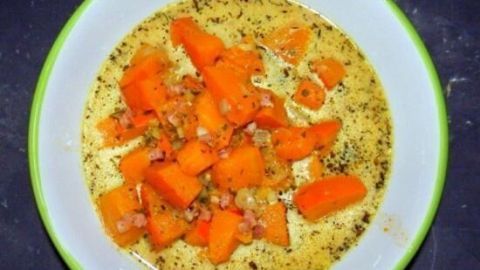 Eine cremige Kürbissuppe mit stückigen Kürbiswürfeln, serviert in einer weißen Schüssel auf einem dunklen Tisch.