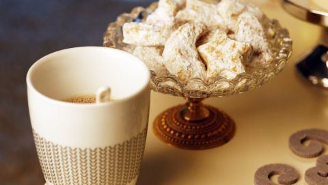Ein Becher mit leckerem Getränk steht neben einer eleganten Schale mit Keksen auf einem Tisch, ideal für den Kinderbesuch.