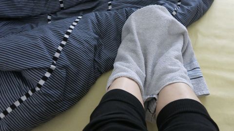 Füße, eingewickelt in ein feuchtes Handtuch, liegen in einem Bett mit blau-gestreifter Bettwäsche, um die Hitze zu lindern.
