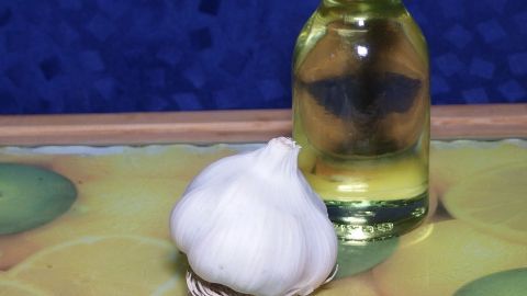 Eine Knoblauchzehe liegt neben einer Flasche Öl auf einem bunten Tisch. Sie symbolisieren die Zubereitung von Knoblauchöl.