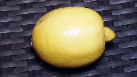 Eine frische, leuchtend gelbe Zitrone liegt auf einer dunklen, geflochtenen Unterlage und scheint bereit zur Verwendung in einem Duftweichspüler.