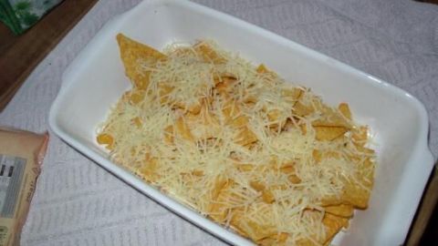 Überbackene Tortilla-Chips, bedeckt mit geschmolzenem Käse, liegen in einer weißen Auflaufform auf einem Tisch.